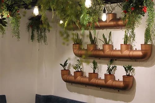 Copper wall shelves holding small potted plants under hanging greenery and filament bulbs