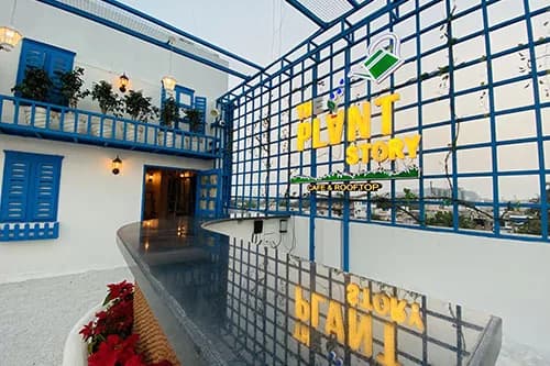 The Plant Story sign on a blue lattice above the white rooftop with blue shutters and red flowers