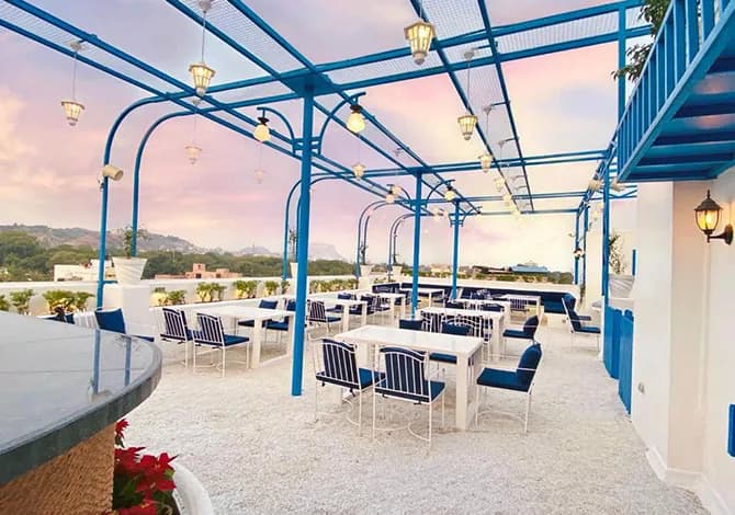 Rooftop terrace at The Plant Story with a blue steel pergola, lanterns and tables set at sunset